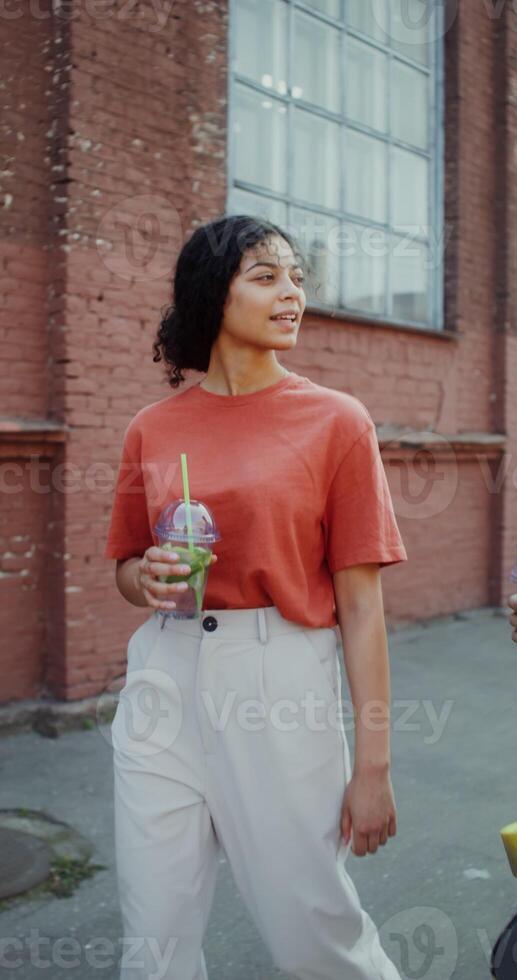 A young man and a woman smile, talk and drink lemonade while walking around the city. A man holds a longboard in his hands - lemonade photo