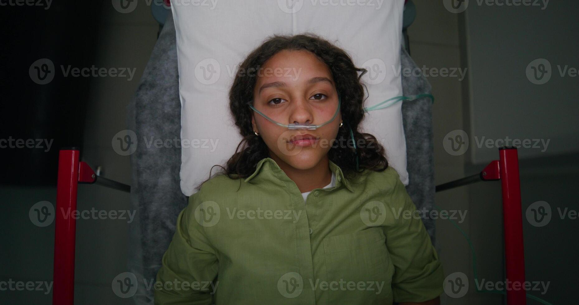 A woman with a breathing tube in her nose is lying on a gurney, top view. She is being driven down the hospital photo