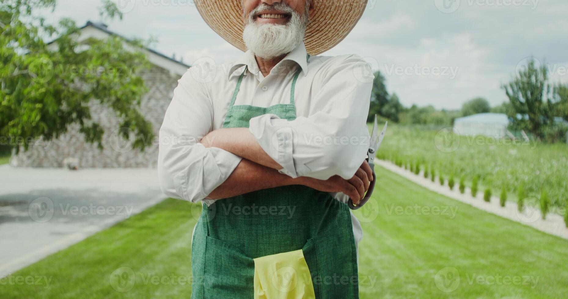 An elderly man with a gray beard, dressed in an apron and hat, smiles while looking at the camera, crossing his arms on his chest photo