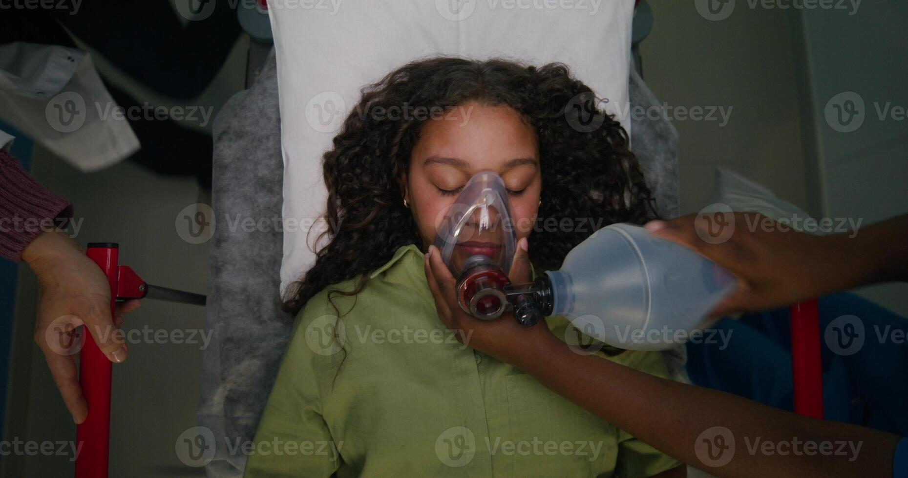 The patient is lying on a gurney with her eyes closed. The nurse gives her air through an oxygen mask photo
