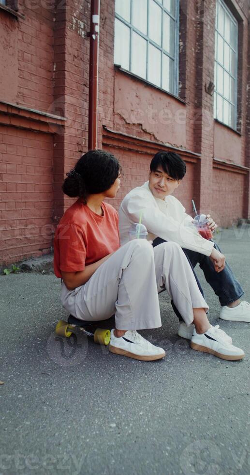 A young man and a woman are talking and drinking lemonade while sitting on a skateboard on a city street - lemonade photo