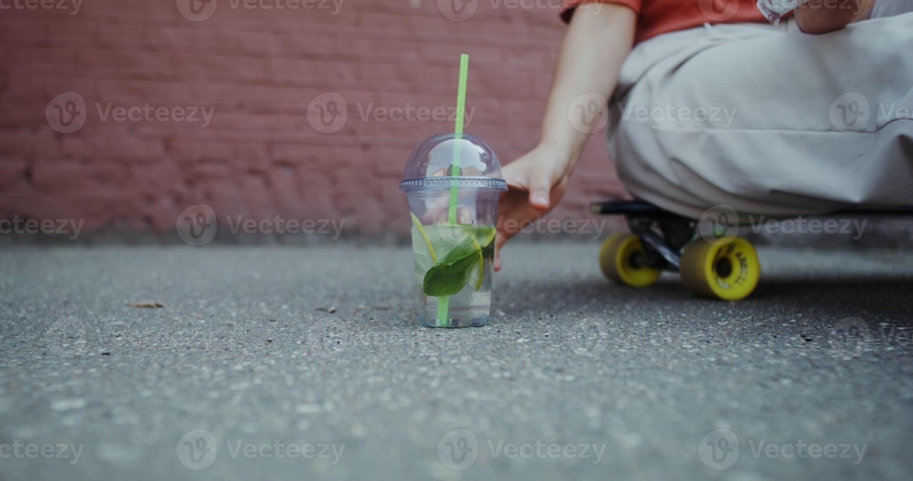 A woman's hand takes a disposable mojito cup with a straw standing on the asphalt, there is no face photo