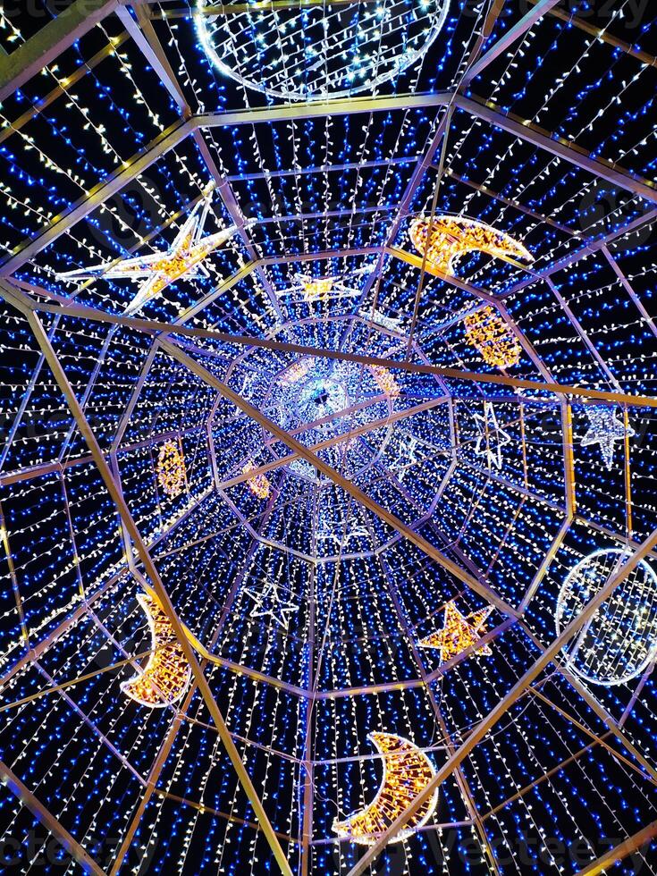 Stunning low-angle view of a dazzling light installation. Blue and warm-white LED lights adorn a geometric framework, creating stars and crescent moons. photo