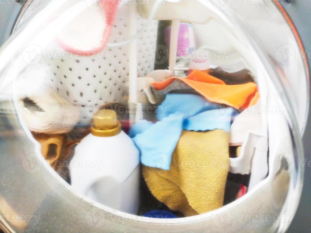Laundry machine with clothes and cleaning product. Represents chores, routine, domesticity, and cleanliness. Use for articles on home life, cleaning, and lifestyle topics. photo