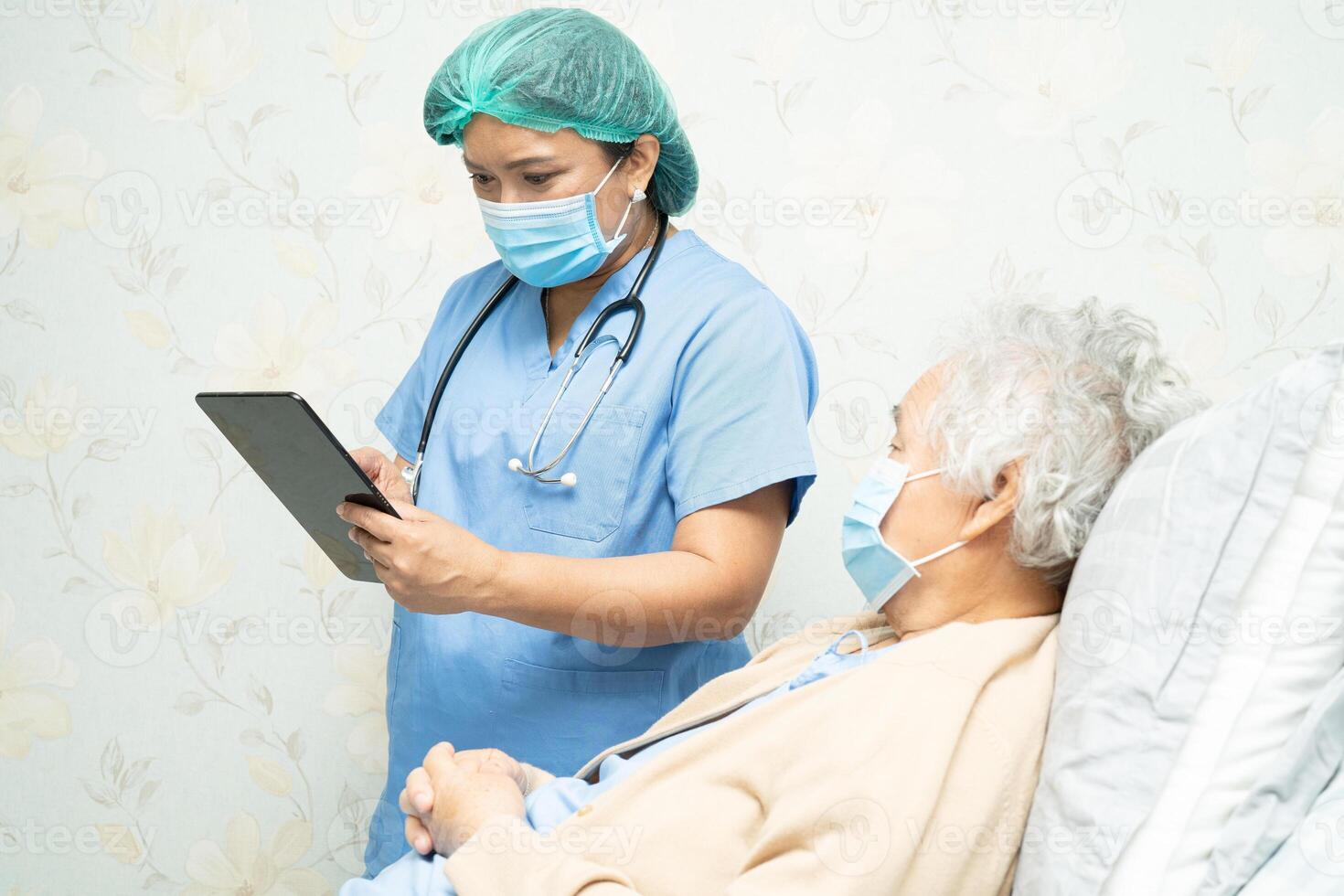 Doctor wearing face shield and PPE suit new normal holding digital tablet to search data about infection, kill and treat Novel Coronavirus with old patient photo