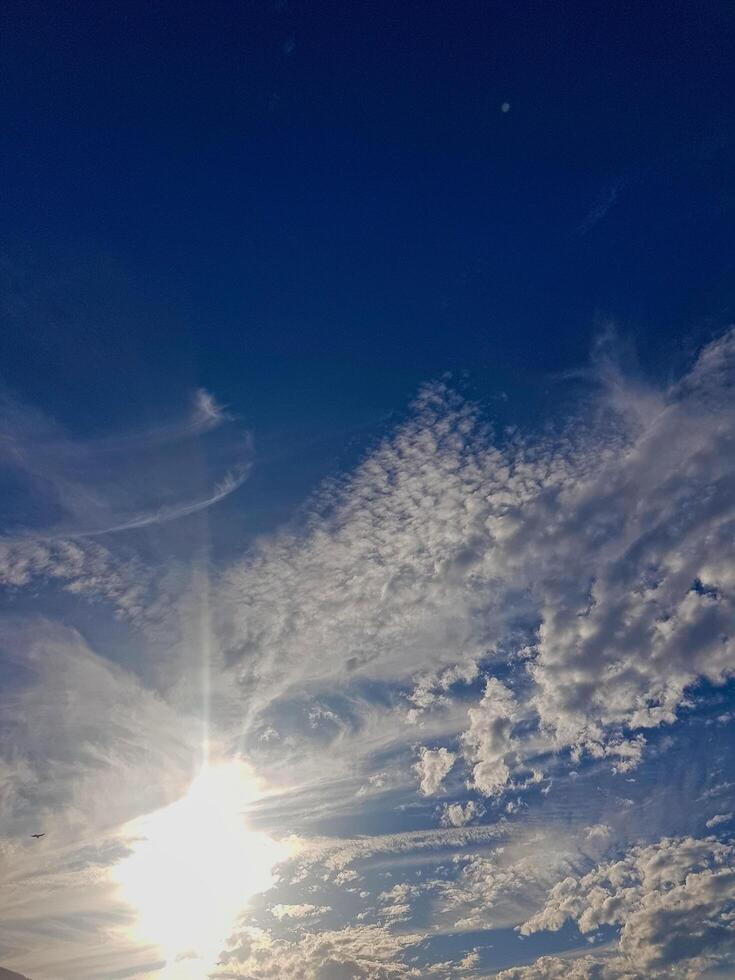 Celestial Canvas - A clear blue sky adorned with fluffy white clouds, where sunshine radiates from behind and casts a warm, inviting glow across the horizon. photo