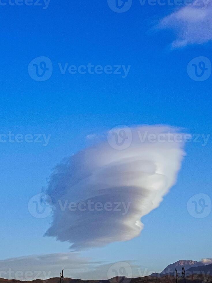 Against the brilliant canvas of a crystal-clear blue sky, a majestic cloud formation unfolds, its dramatic contours and shapes starkly defined, evoking the ominous presence of an impending storm photo