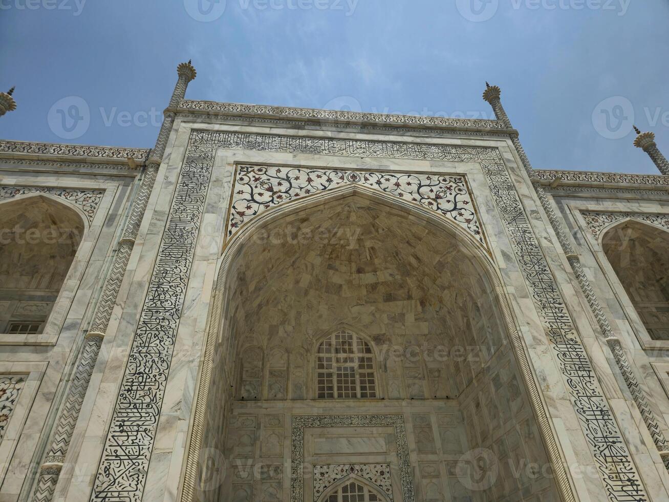 This is a closer upward view of one of the main archways of the Taj Mahal. The intricate inlay work in black marble, featuring Arabic calligraphy and floral motifs, photo