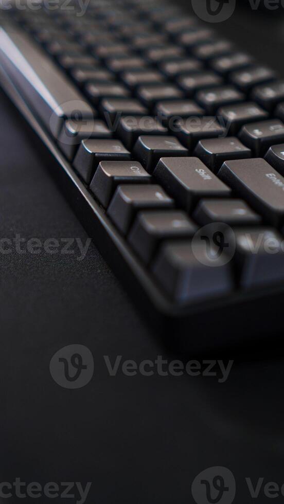 A close-up of a sleek black keyboard with square keys, resting on a dark, textured surface. The keyboard's sharp angles and minimalist design photo