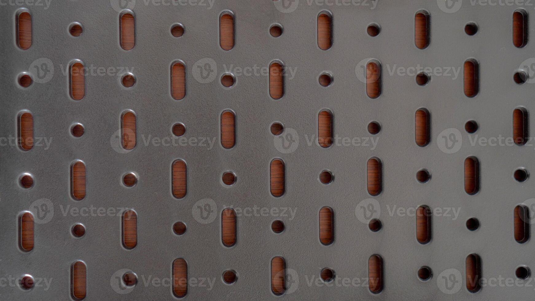 A close-up of a perforated metal surface with a repeating pattern of oval and circular holes. The dark, industrial aesthetic creates a sense of mystery and intrigue photo