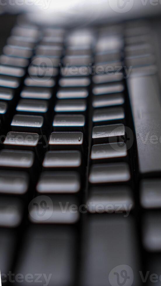 A close-up of a sleek black keyboard with square keys, resting on a dark, textured surface. The keyboard's sharp angles and minimalist design create a modern photo