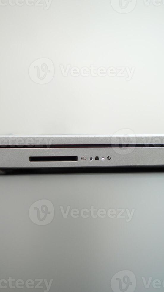 Close-up of a sleek silver laptop with a visible SD card slot and power button. The laptop rests on a clean, white surface. photo