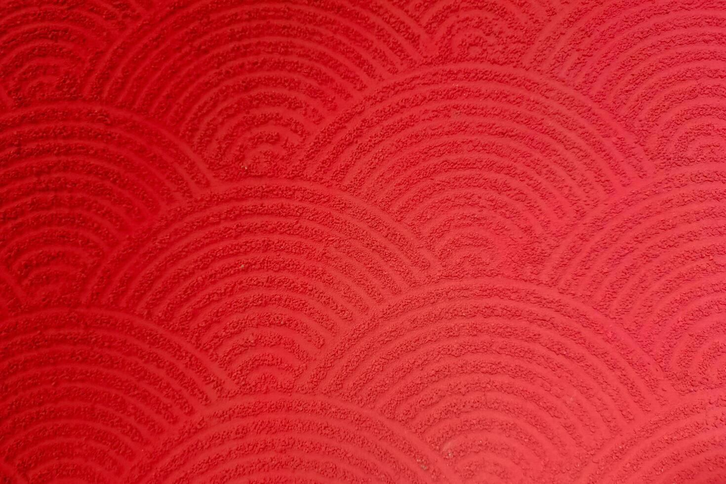 Red textured surface with repeating semi-circular wave patterns, resembling traditional Japanese motifs. photo