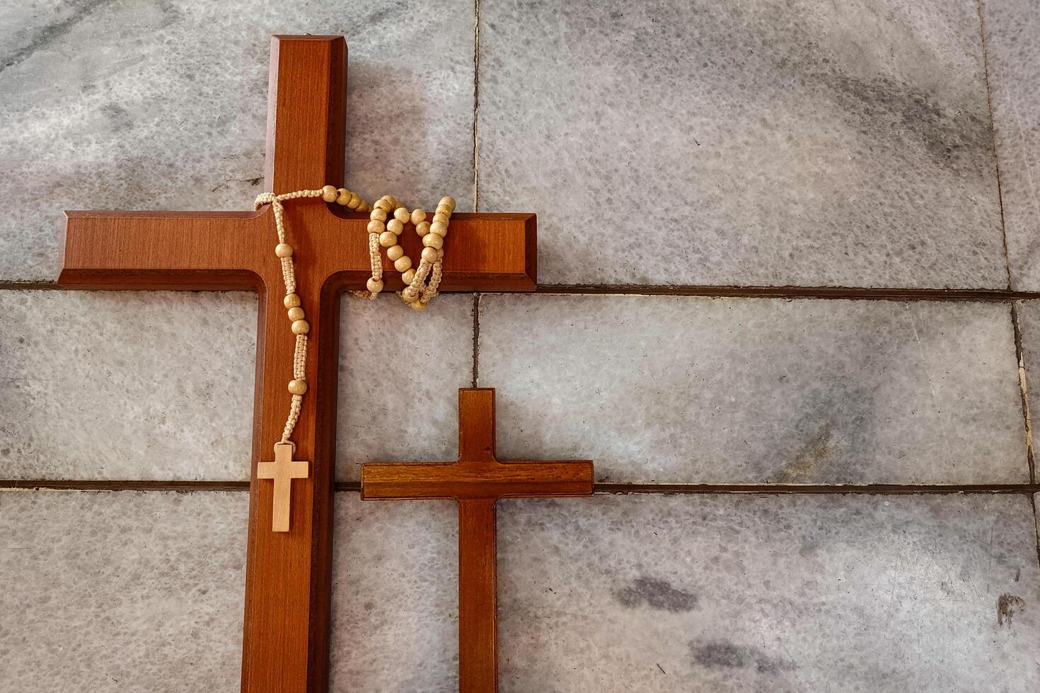 Two wooden crosses and a rosary rest on a marble-tiled surface. photo