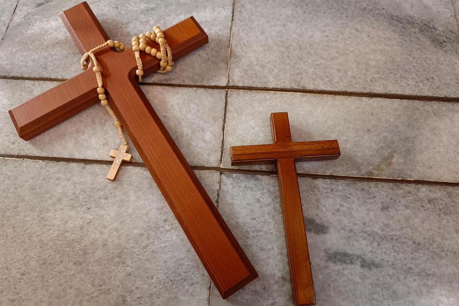 Two wooden crosses on a tiled floor, one with a rosary draped over it. photo