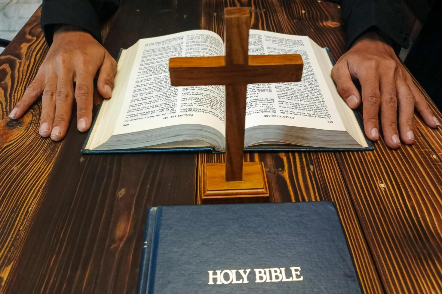 A wooden cross stands between two Bibles on a wooden table. photo