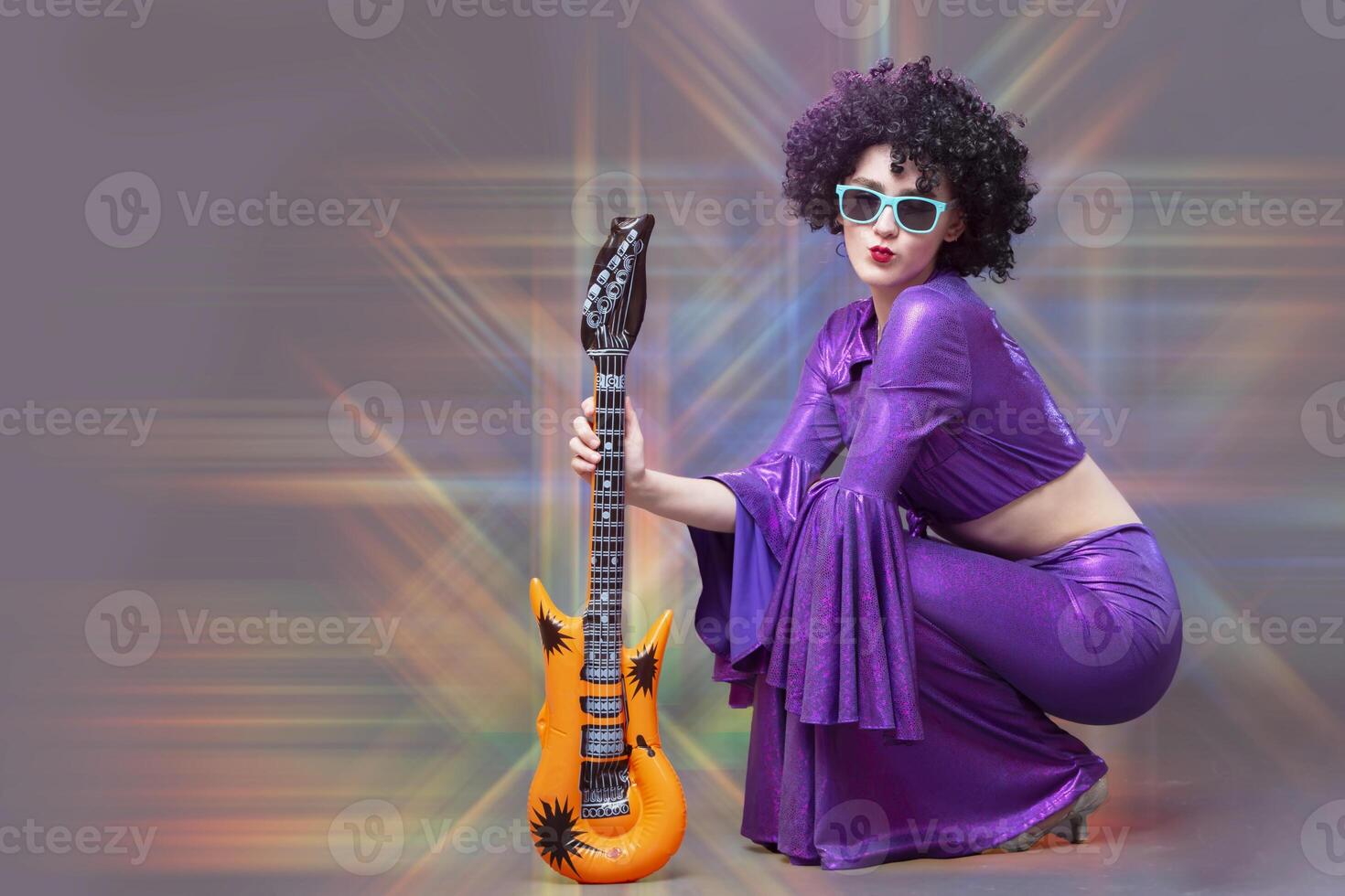 Funny girl disco singer in a black curly seventies style wig posing in the rays of stage light. photo