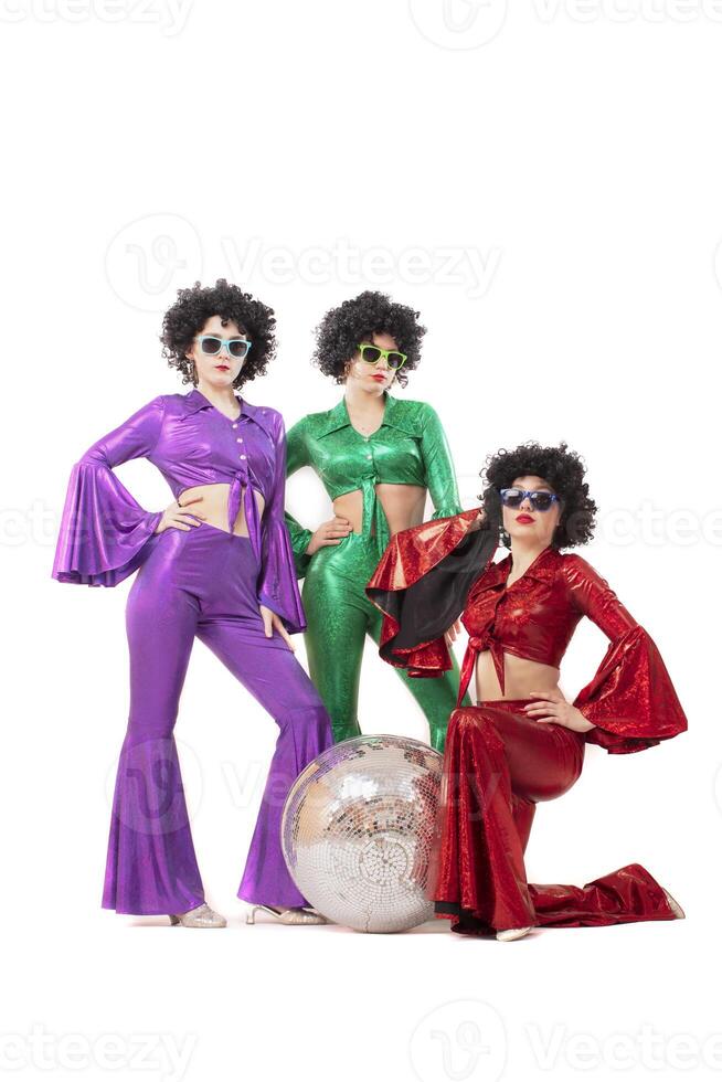 Three female pop stars in neon clothes pose in front of a silver ball. photo