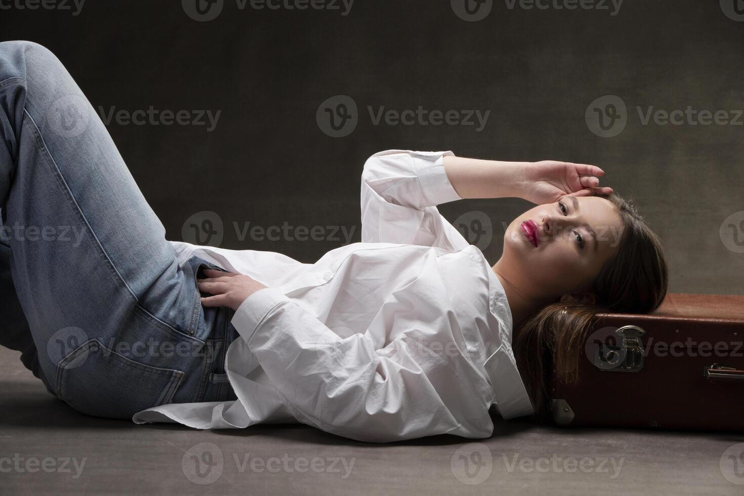 A beautiful girl lies on an old suitcase on a gray background photo