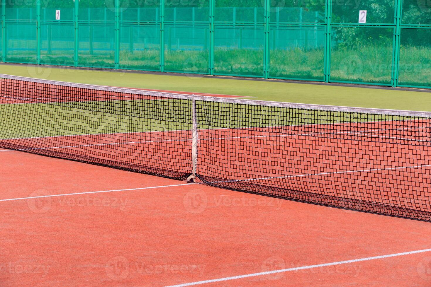 The tennis court is empty with a net and a green fence photo