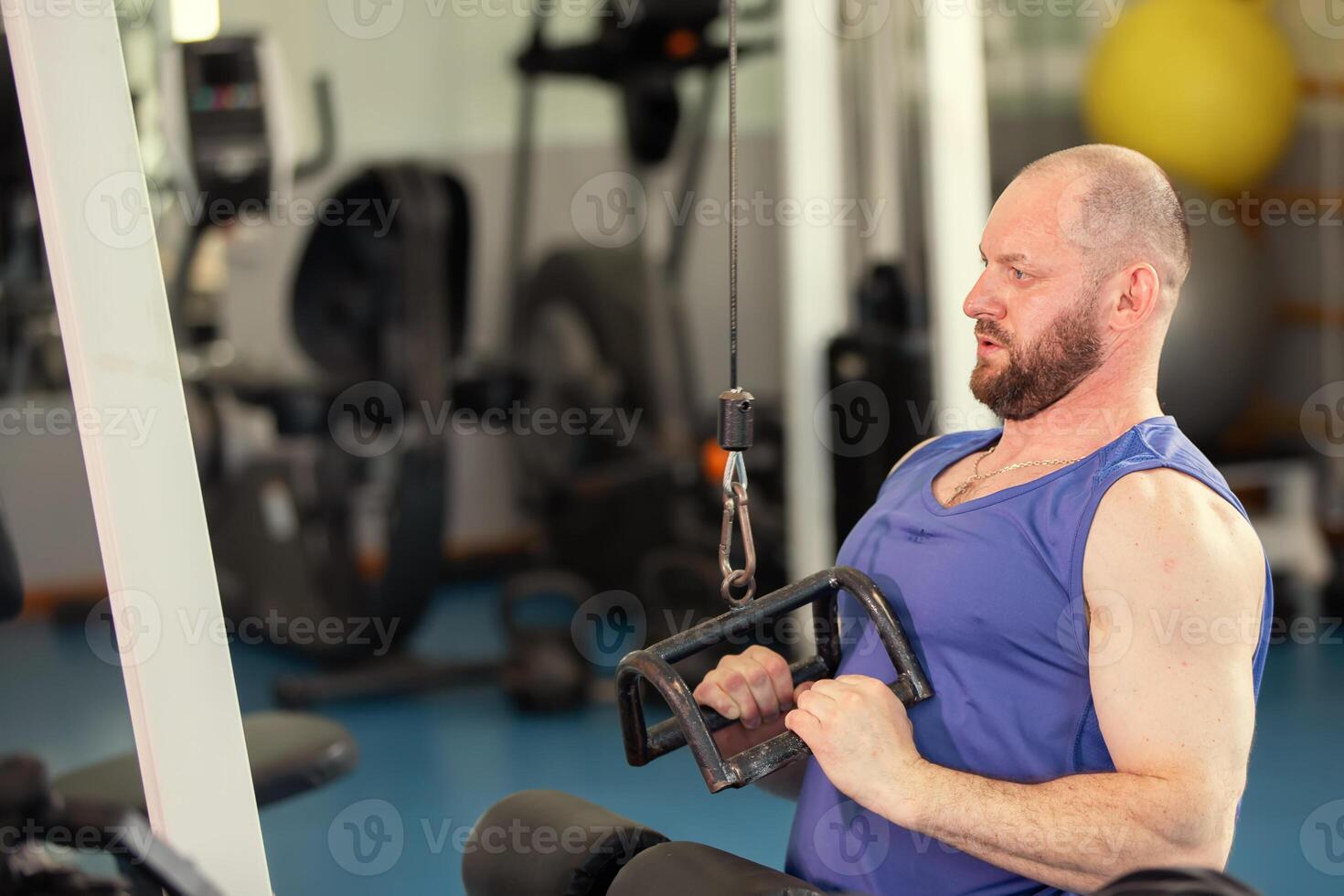 A male athlete is working out on a weight training machine in a gym. He is focused on doing the exercise. photo