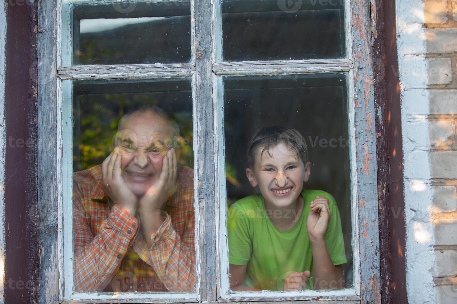 Grandfather and grandson look out of the window of a village house and grimace. Father's Day. photo