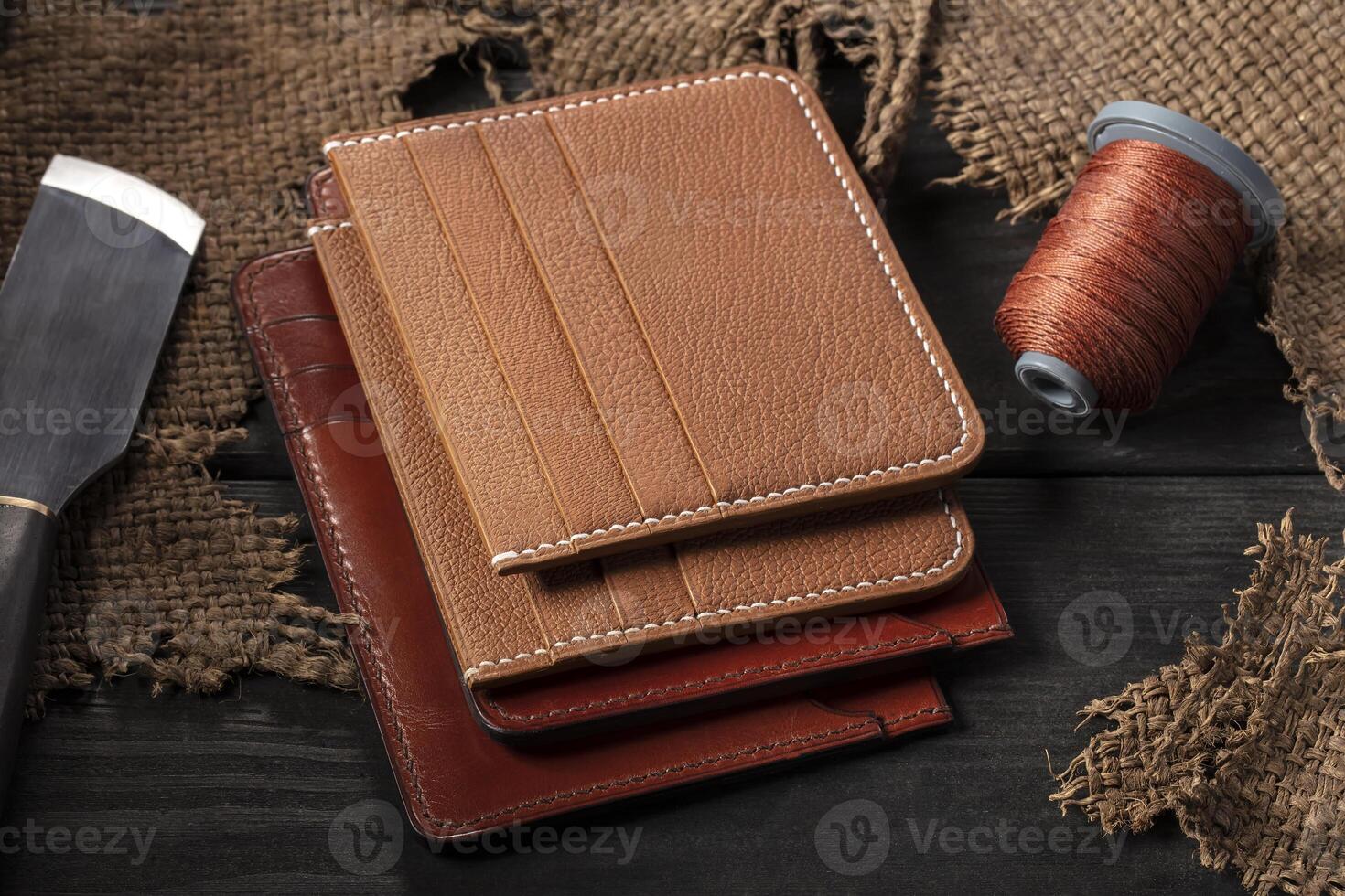 On a wooden table there are leather wallets, a spool of thread and a knife. photo