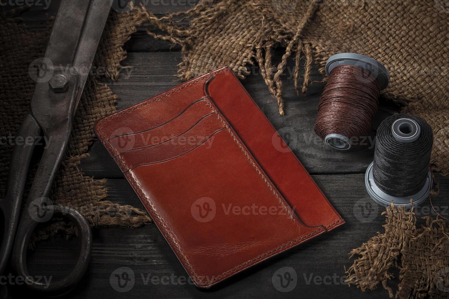 On a wooden table there are leather wallets, a spool of thread and scissors. photo