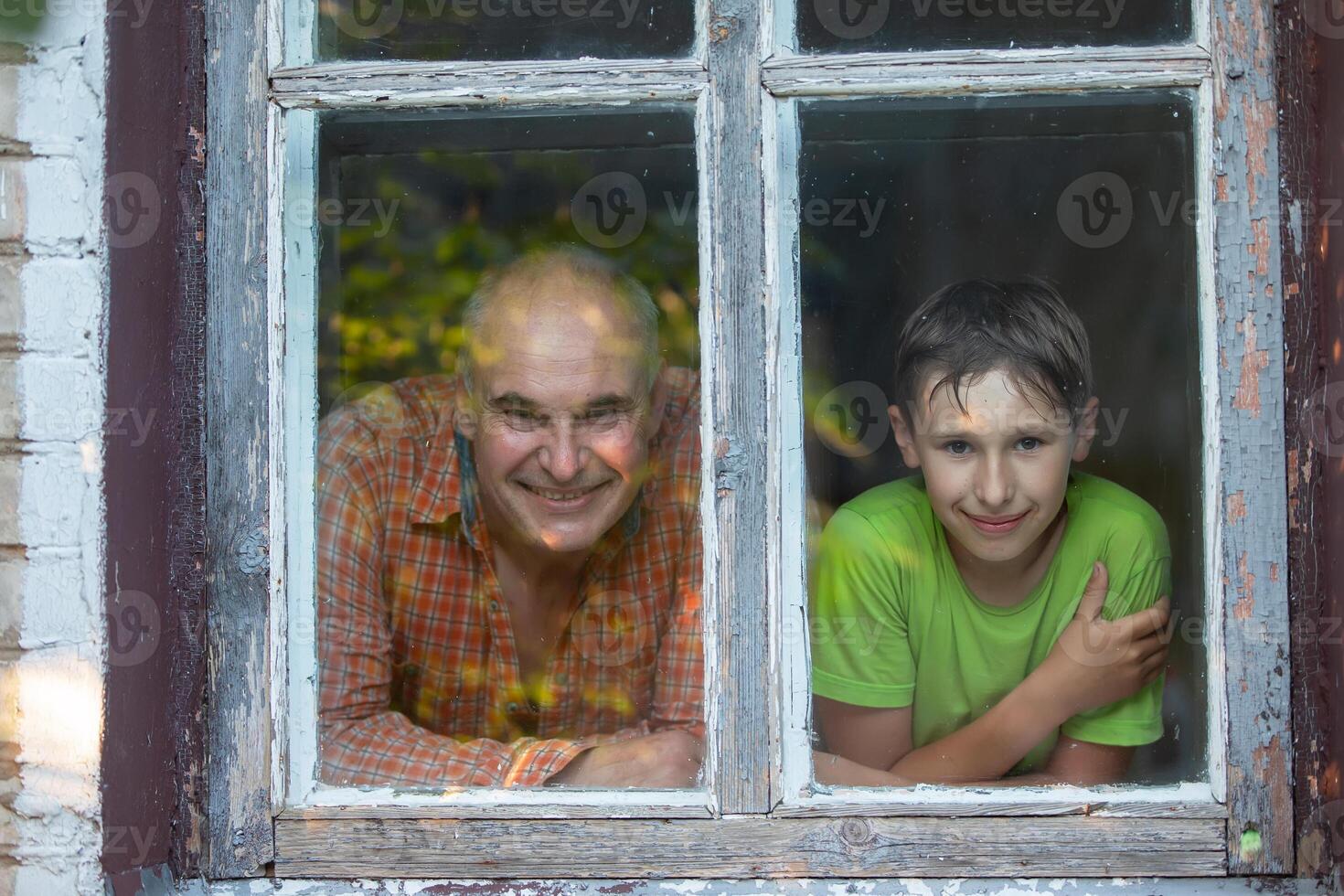 Grandfather and grandson looking out of the window of a village house and smiling. Father's Day. Boy and man in the window. photo