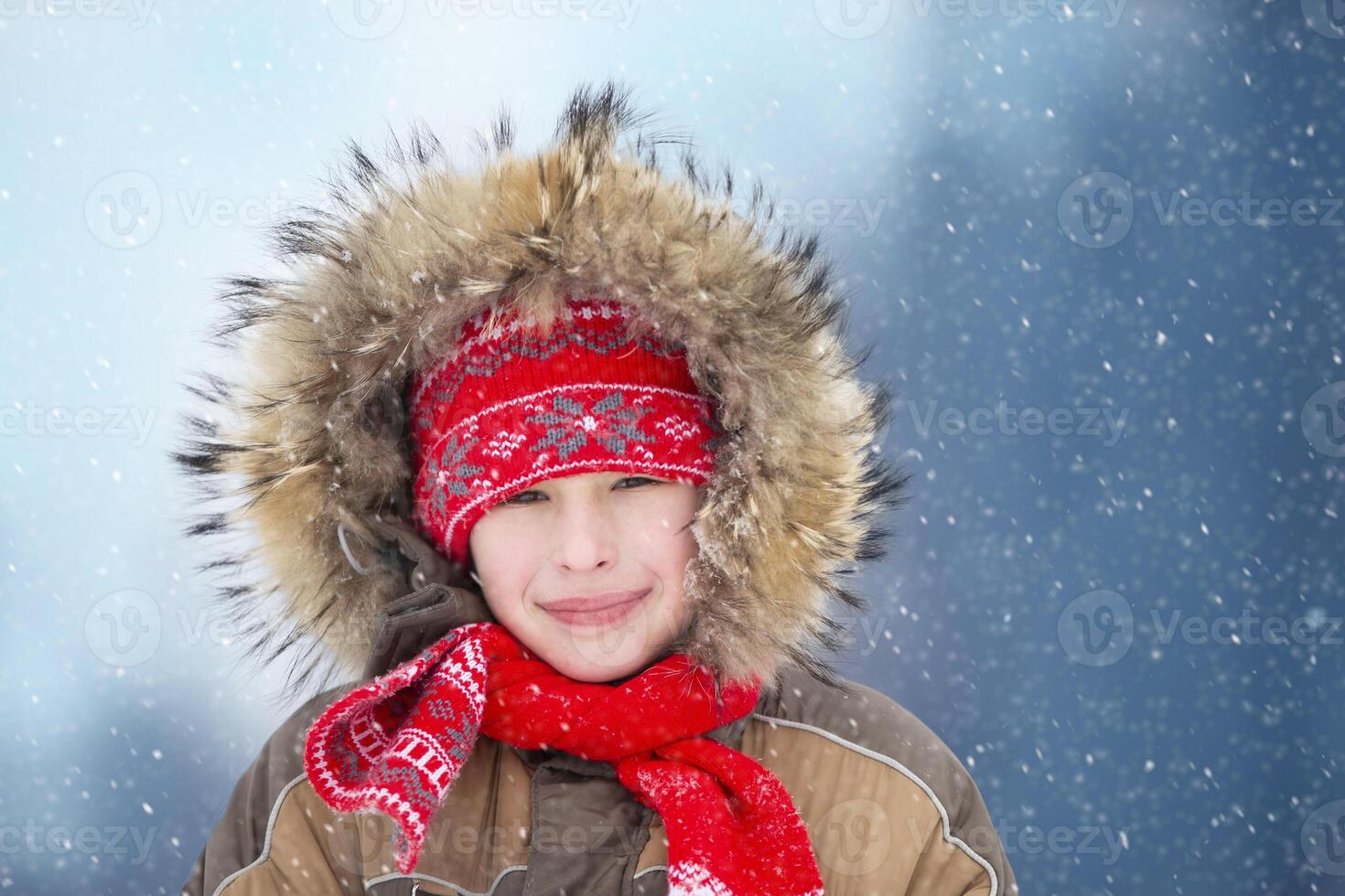 A boy in the winter in a warm fur hood against the background of falling snow. Portrait of a child in winter. photo