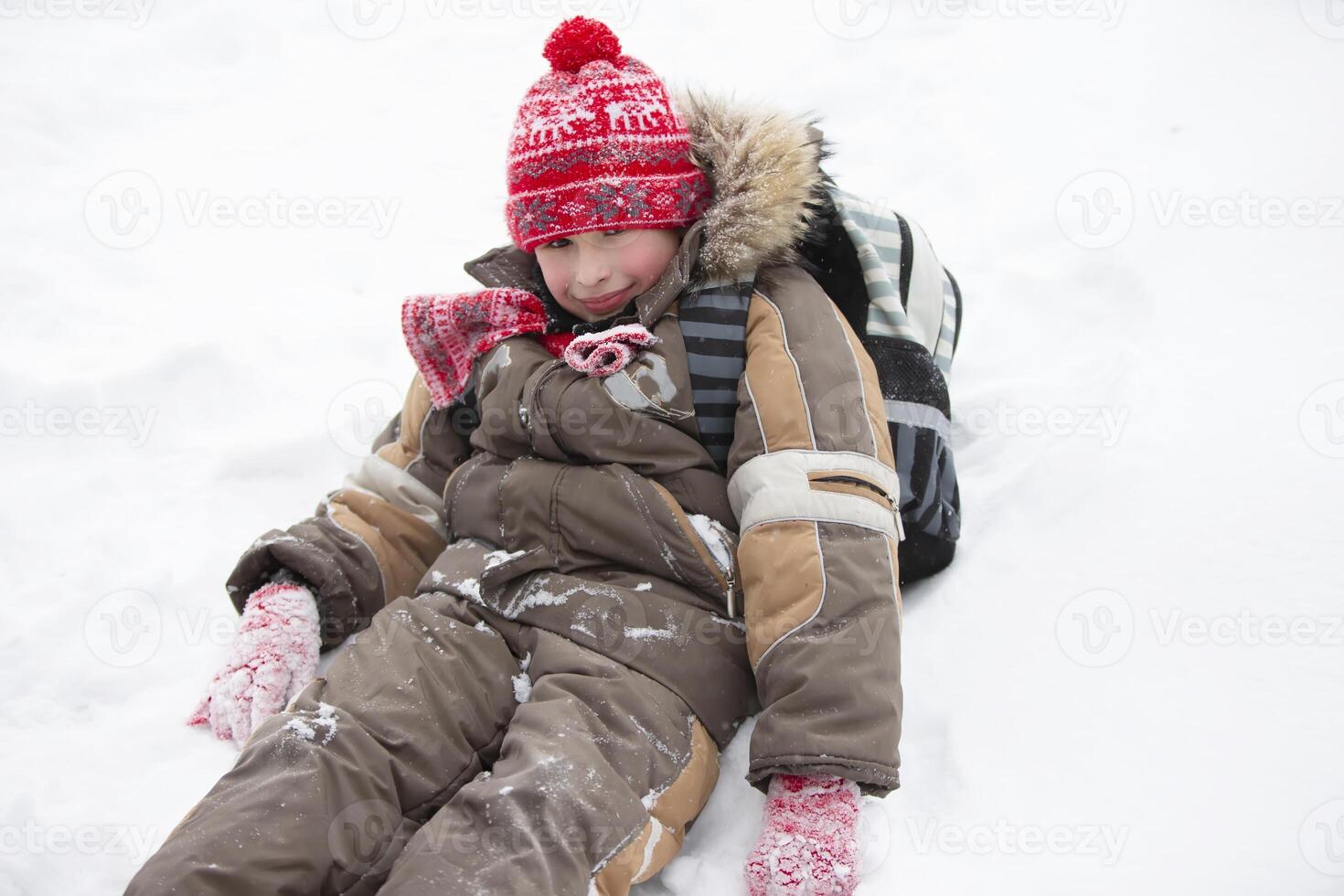Funny boy in winter goes to school with a backpack.A little boy with a schoolbag sits in a snowdrift. photo
