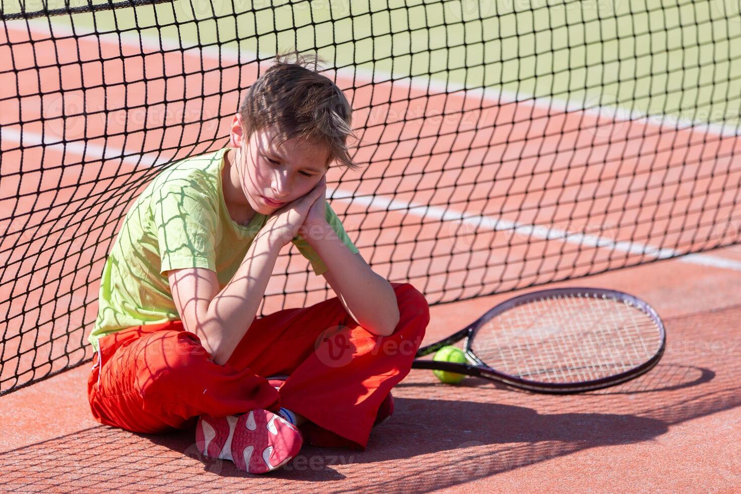 The boy lost the tennis competition The child sits at the net with a racket. Psychology of sports in childhood. photo