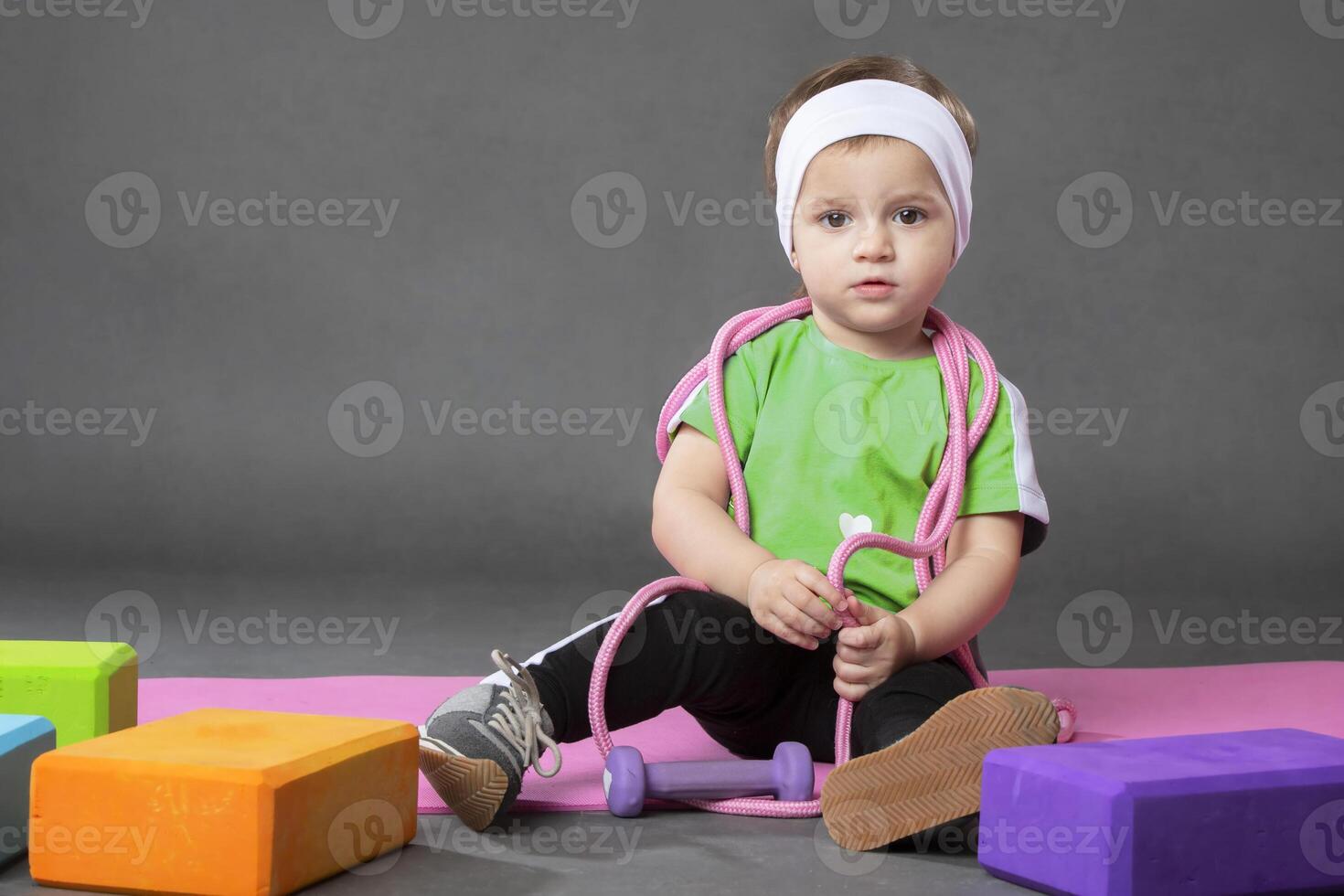 Two year old girl doing sports posing with skipping rope and ball on grey background.Sports activities with little kids. photo