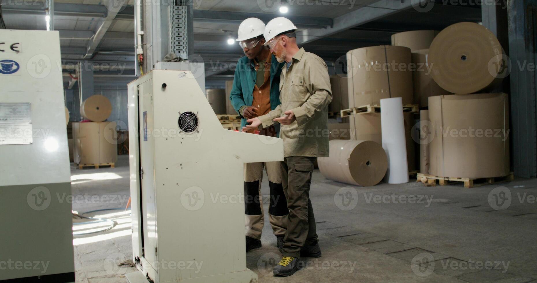 Industrial scene with two men in protective gear talking beside a machine control panel at a paper mill. photo