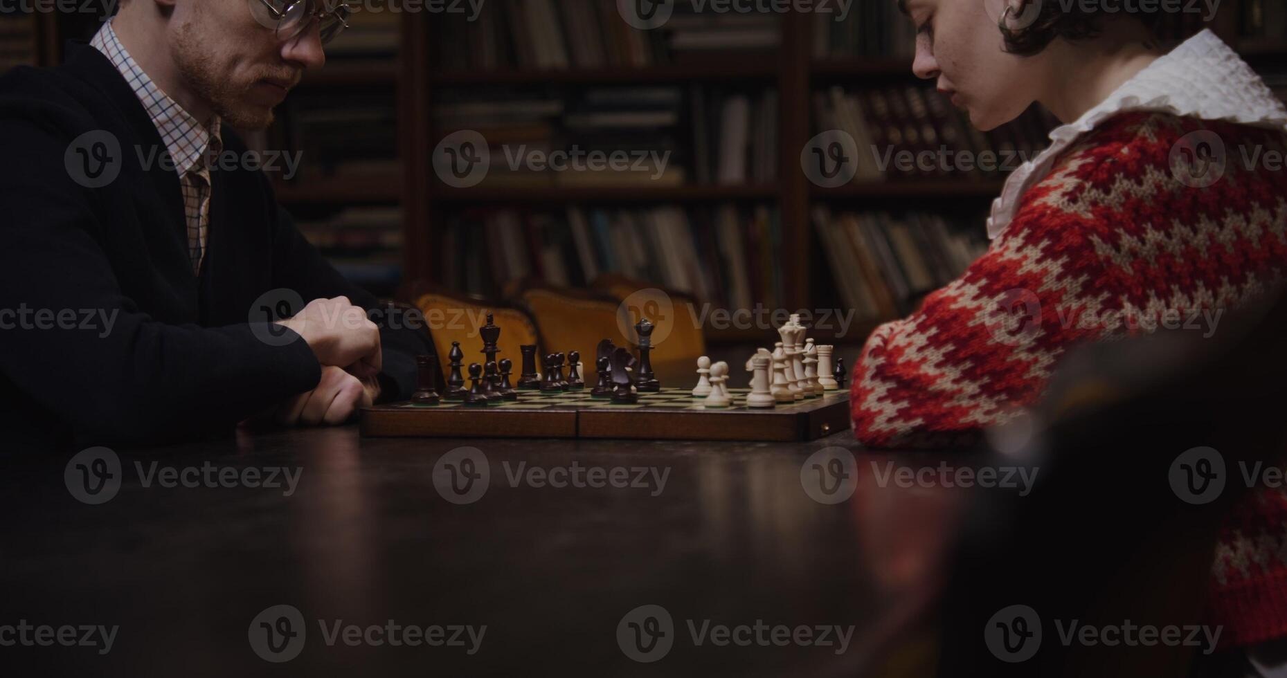 Intellectual young couple engaged in a strategic chess match across a library table. photo