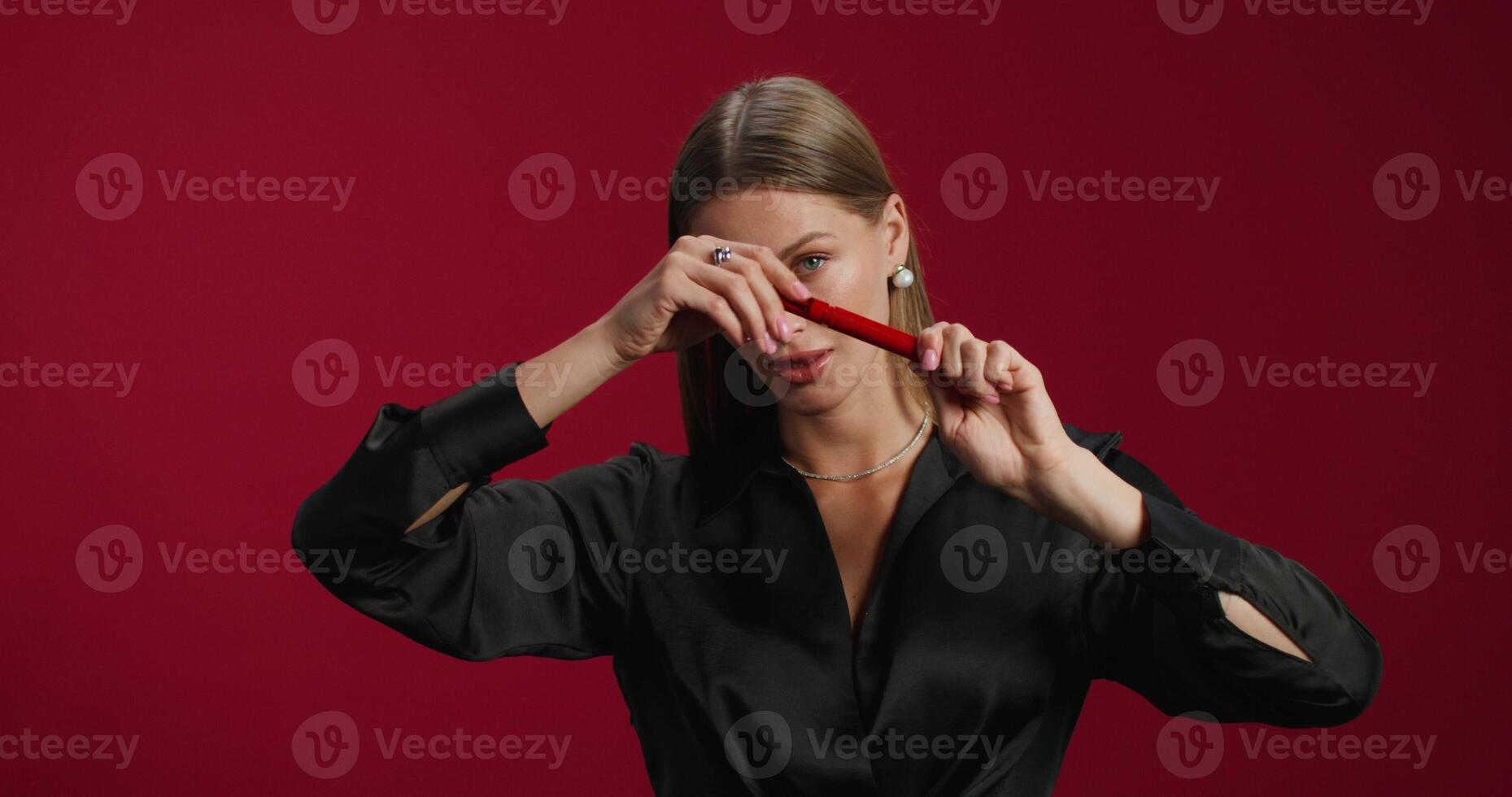 A woman paints her eyelashes with mascara. She smiles at the camera standing in the studio background. photo