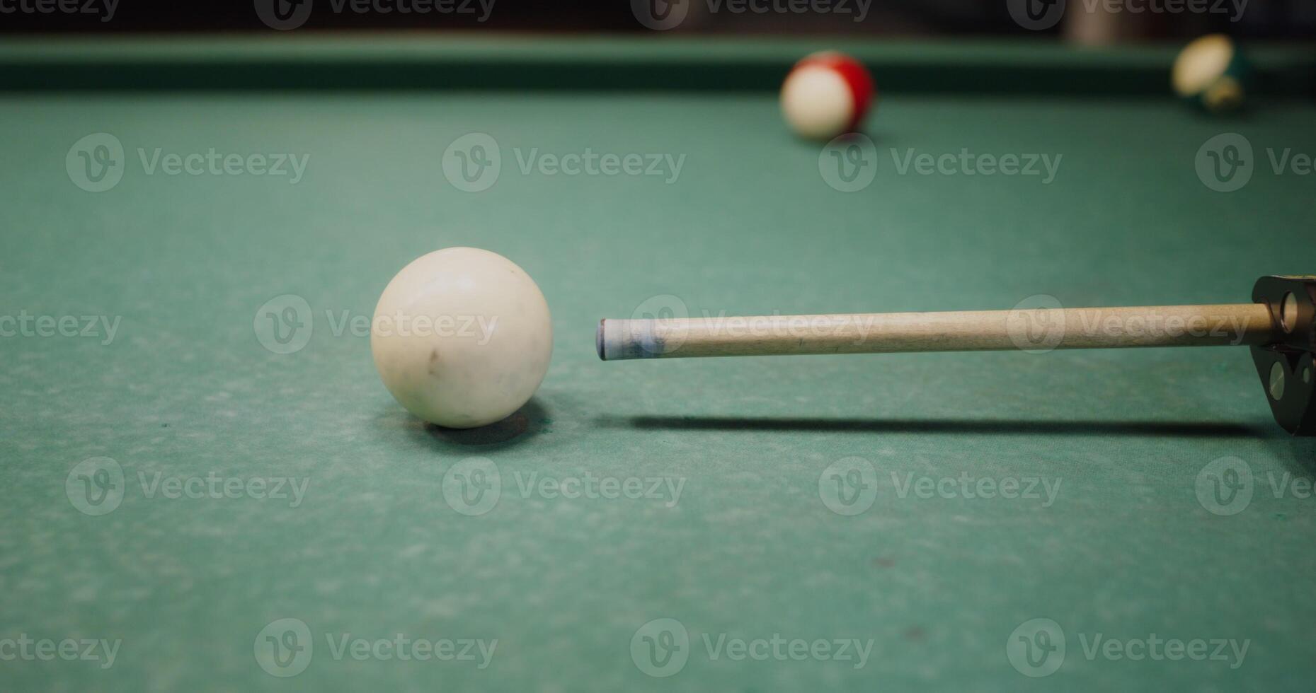 cue is aiming at the white ball lying on the billiard table, close-up, the camera repeats the movements of the cue photo