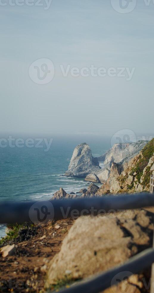 Panoramic view of the sea washing rocky shores and ledges. View from the top of the mountain from the observation deck through the fence, vertical photo