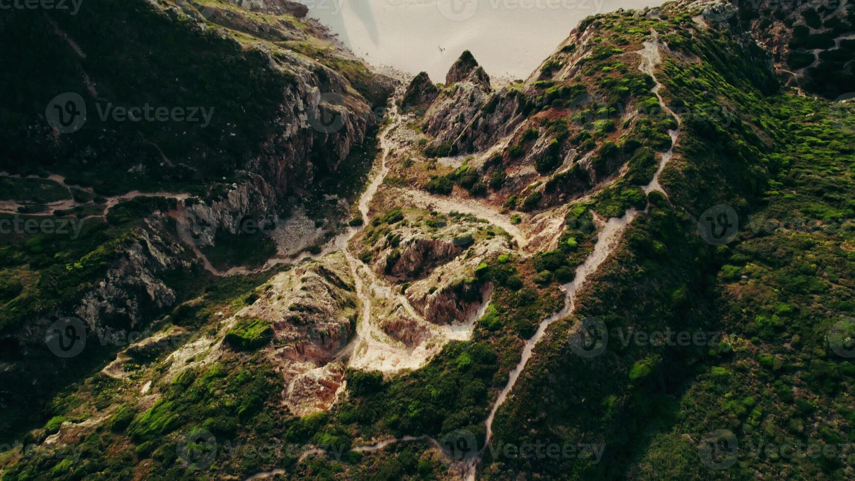 Drone flies over a mountain, a sandy beach with rocks sticking out of the water and moves to a view of the sea photo