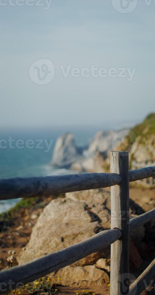 Sea washing rocky shores and ledges. View from the top of the mountain from the observation deck through the fence, vertical photo