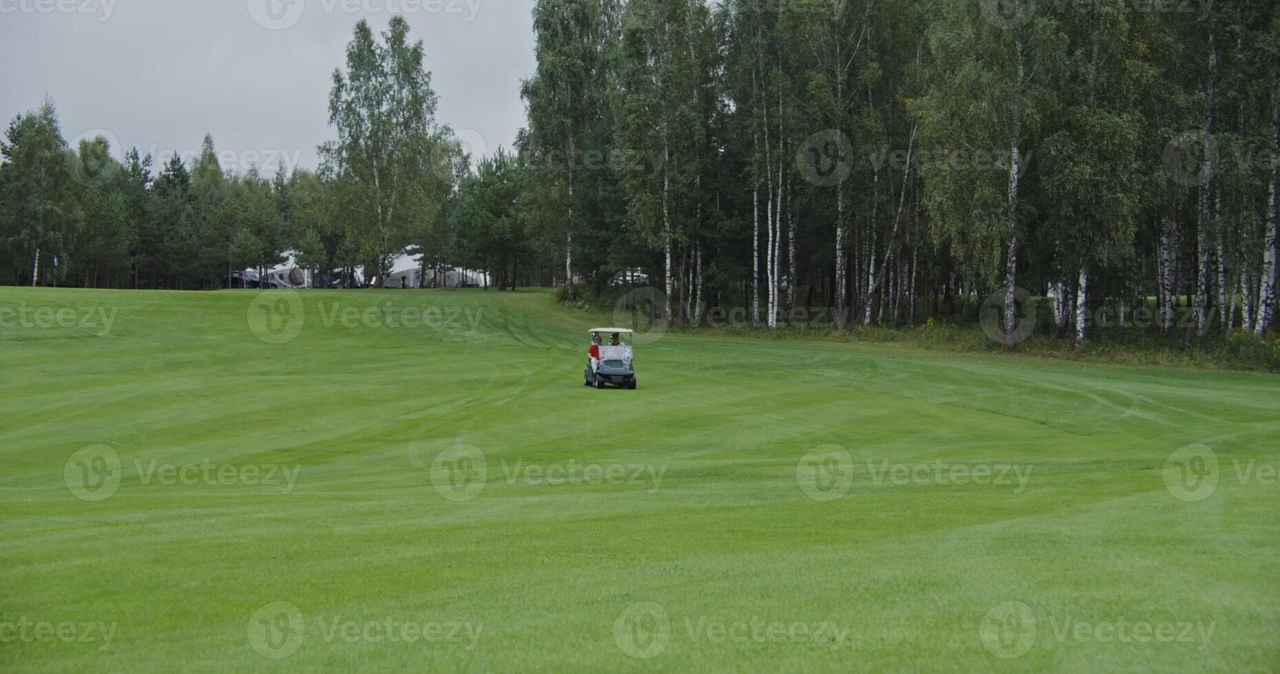 Panoramic view of golf course with the golf car driving through it. Two men are about to play golf while moving from place to place in an electric car on a rainy day photo