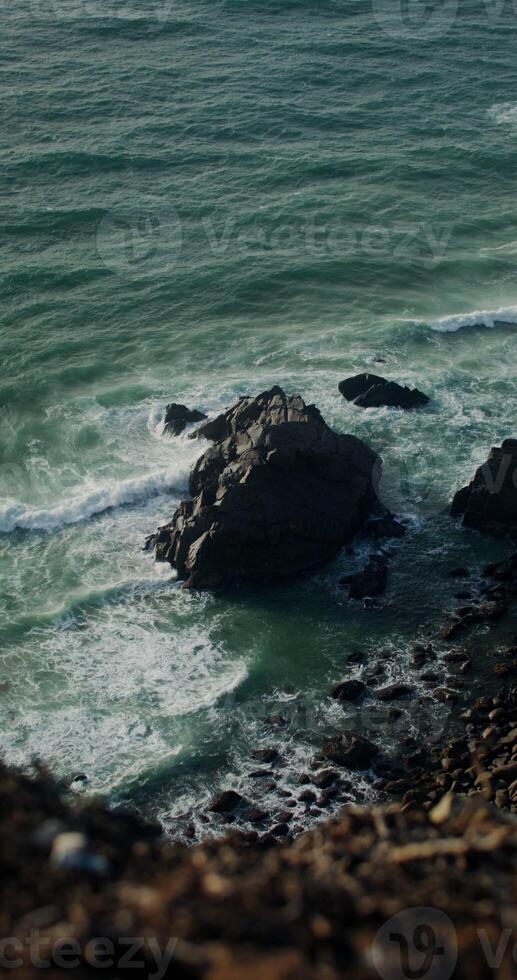 Aerial view of ocean waves hitting the rugged coastline from above. photo