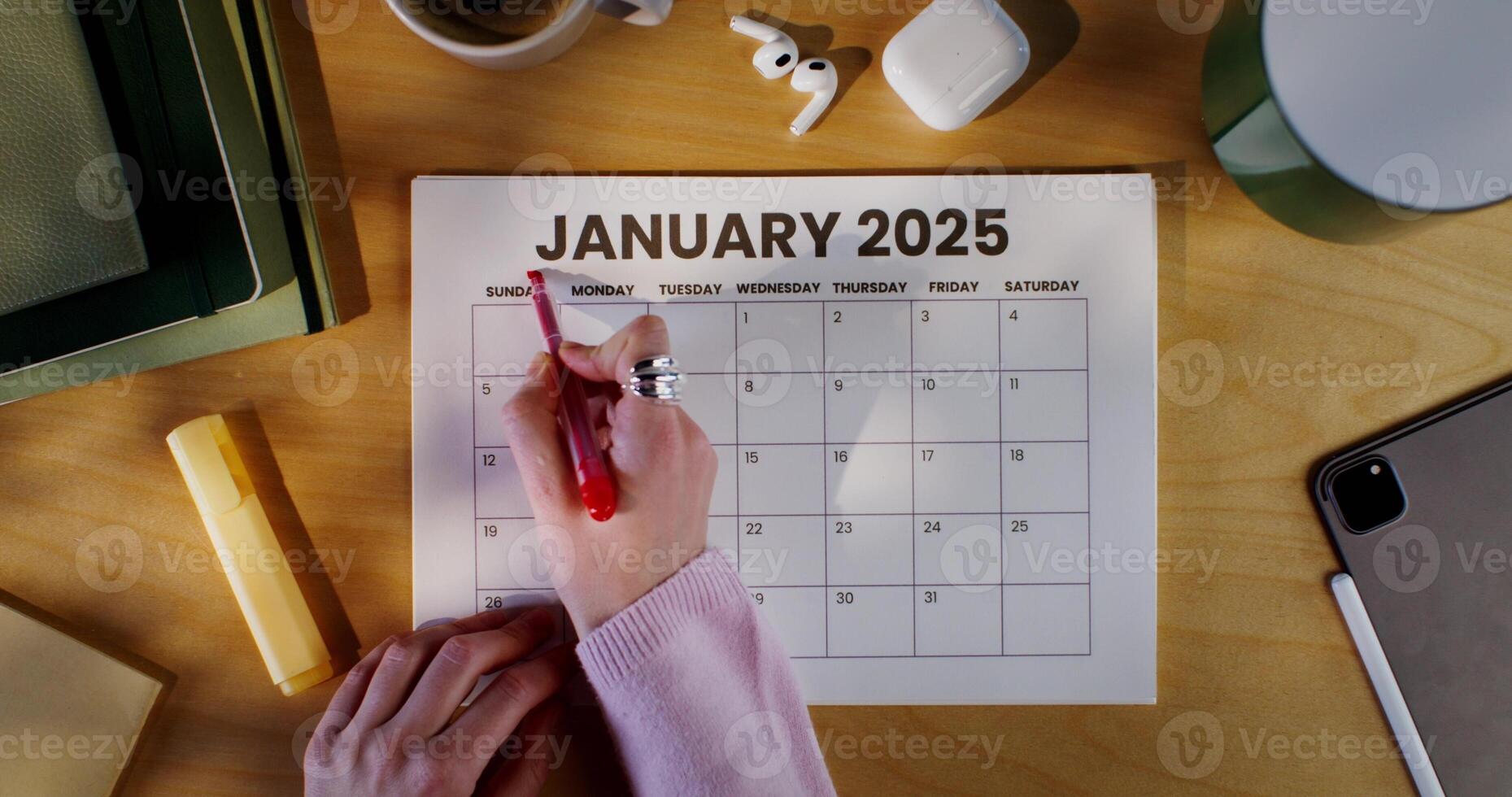 A woman uses a red marker to highlight the month name in her calendar. Zoomed-in view of her hand, person not clearly seen. photo