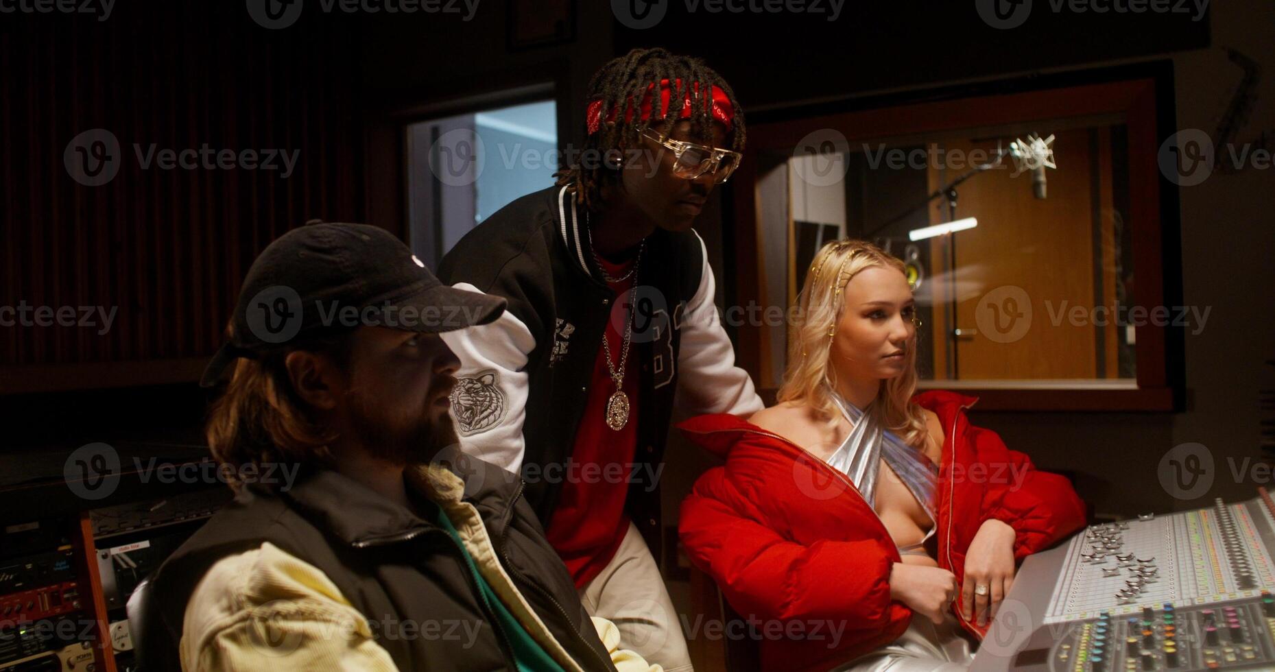 The sound engineer talks to the musicians after recording the song in the studio. They are sitting in front of the equipment photo