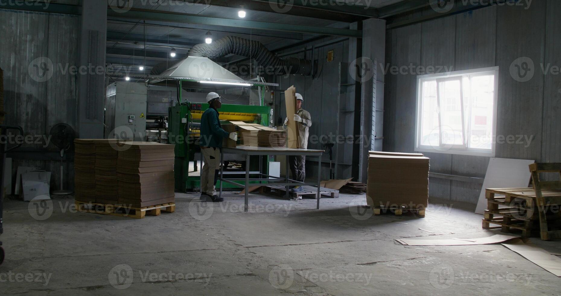 Two men work in a cardboard factory. They take the cardboard cut by the machine and stack it in piles photo