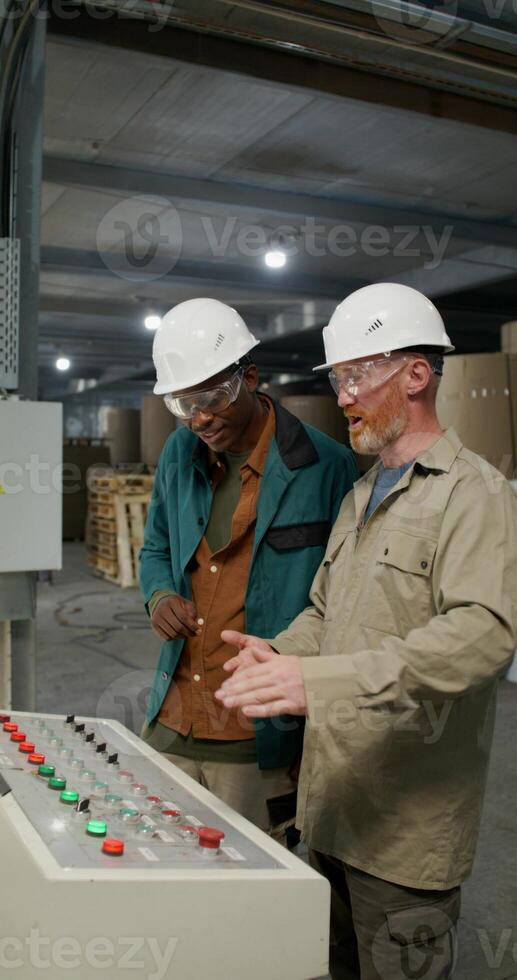 Paper factory interior showing two technicians in helmets and glasses standing by the equipment control panel. photo