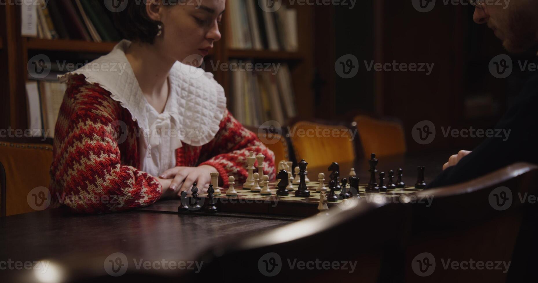Two young adults intensely concentrating while playing chess in a library setting. photo