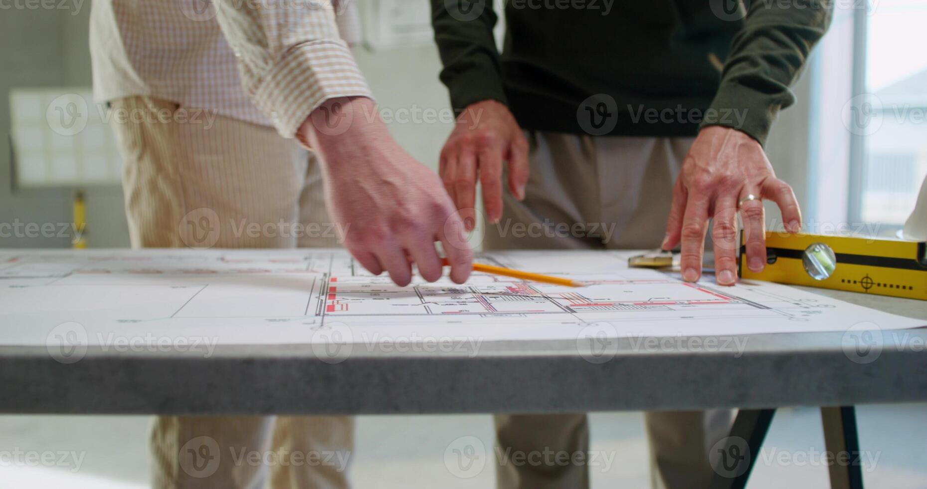 Two men are discussing a house construction project. They are talking standing next to a table in an unadorned room photo
