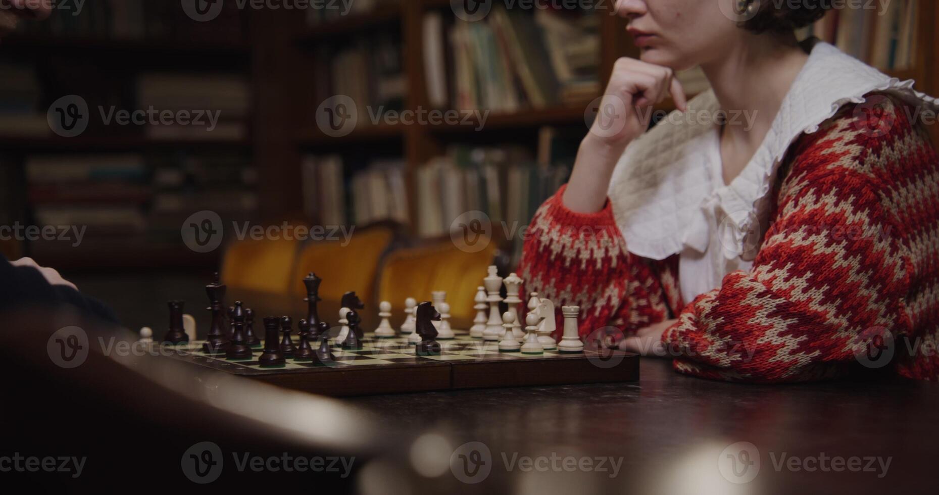 Man and woman of European descent sit across from each other, focused on a chess game in a quiet library. photo