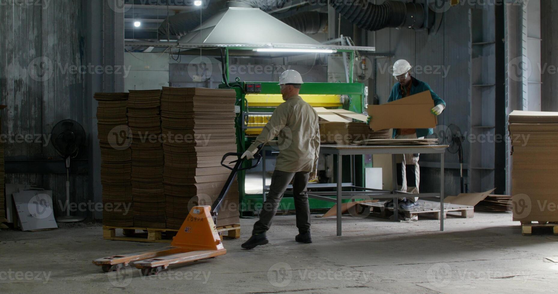 Working in a paper mill. One of the men controls the operation of the machine, the second man loads a stack of cardboard photo